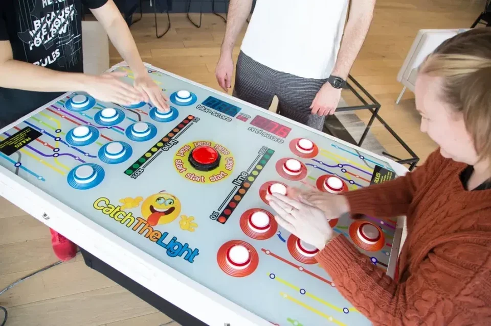 Plusieurs personnes jouent à une borne de jeu interactive de table intitulée **"Catch The Light"**