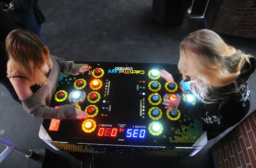 Deux femmes jouent à une borne arcade de table "Catch The Light Combo" en intérieur